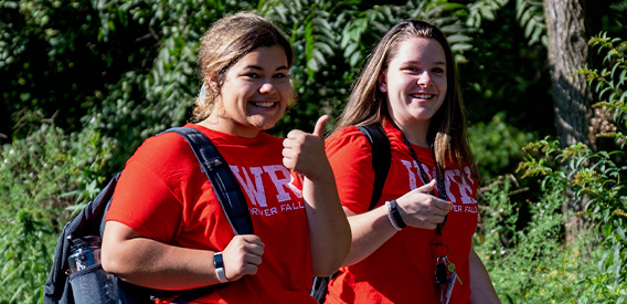 Two students give the camera a thumbs up as they walk around campus