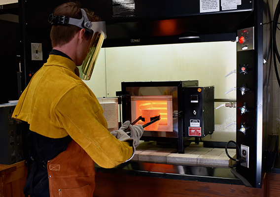 A student wears protective gear while pulling a crucible out of a furnace