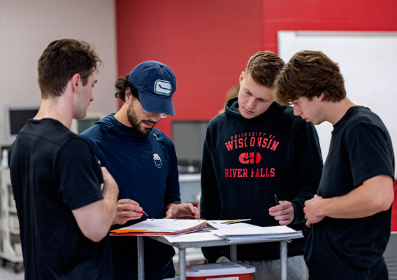 Four male students stand around a table looking at a worksheet