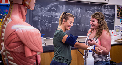 One student puts a blood pressure monitor on the arm of another student during a physiology class