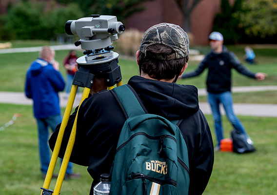 An Engineering student carries surveying equipment around campus