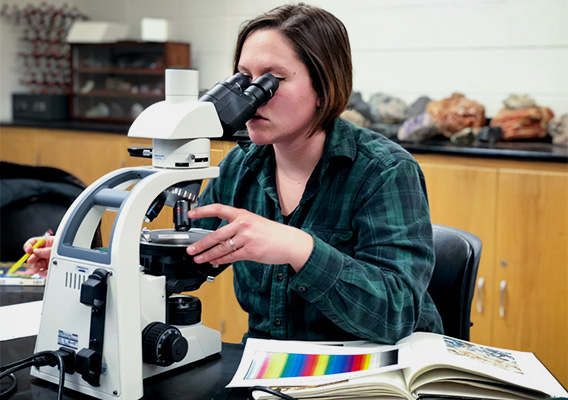 A geology student studies rock colors under a microscope