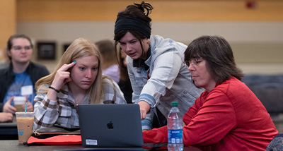 An Admissions Adviser points to a laptop screen with a student and parent during an orientation session
