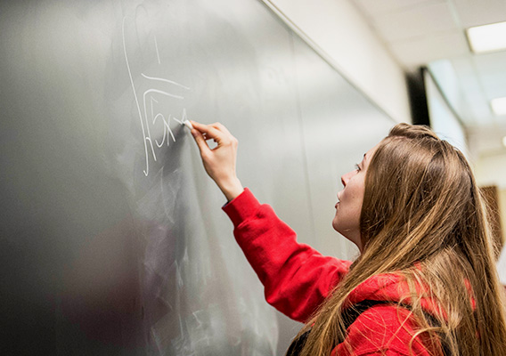 Math student writes an equation to solve on a chalkboard