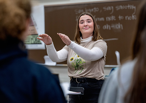 A female student practices conducting in front of fellow classmates
