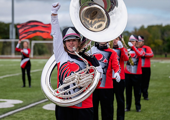 A female tuba player raises their fist in celebration during a marching band performance at the UWRF football stadium. 