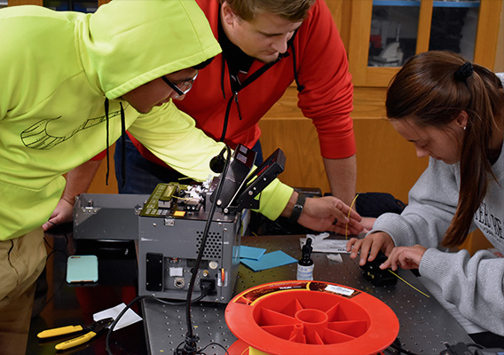 Three students work with 3D printing filament in an engineering lab